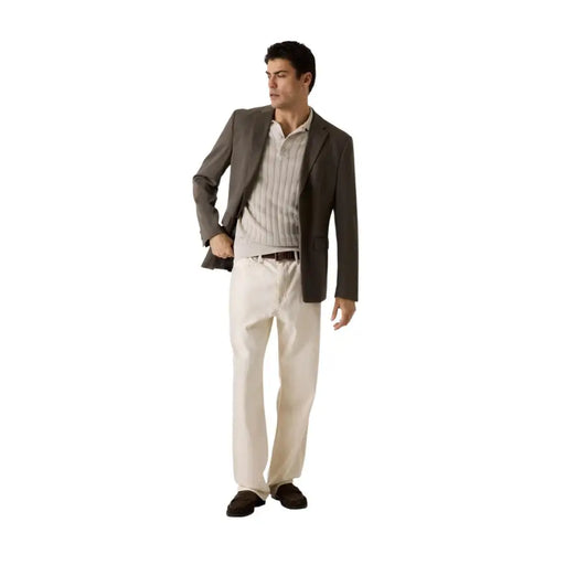 Ein Mann, der einen Guess Beigefarbenes Herren-Poloshirt mit kurzen Ärmeln aus Baumwollviskose, kombiniert mit einem dunkelgrauen Blazer und cremefarbenen Hosen.