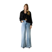 Eine Frau, die Guess Weite, locker sitzende blaue Jeans aus Lyocell-Mischgewebe für Damen, kombiniert mit einer schwarzen Rüschenbluse mit transparenten Ärmeln.