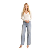 Eine Frau trägt eine guess Weißer Damenpullover aus Viskosemischung mit V-Ausschnitt, cremefarbenen langen Ärmeln und hellblauer, weit geschnittener Jeans.