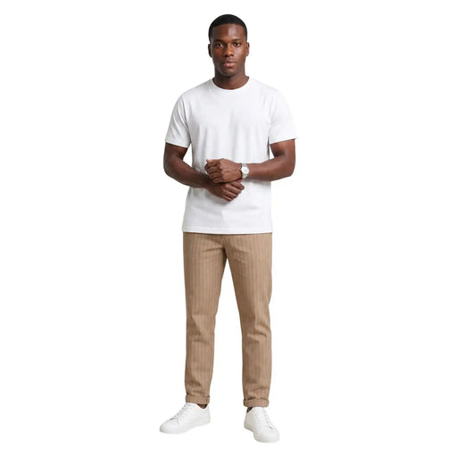 Ein Mann trägt beige gestreifte Baumwollhosen von Hydra Men und ein weißes, kurzärmeliges T-Shirt mit Rundhalsausschnitt. t-shirt und weiße Turnschuhe