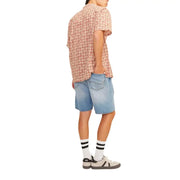 Eine Person, die Jack & Jones Hellblaue Baumwollshorts kombiniert mit einem kurzärmeligen Hemd mit Totenkopfmuster und Knöpfen