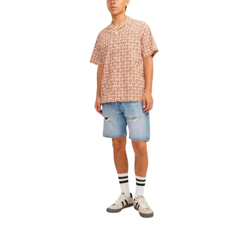 Ein Mann trägt ein kurzärmeliges Hemd mit Totenkopfmuster, kombiniert mit hellblauen Baumwollshorts von Jack & Jones für Herren.