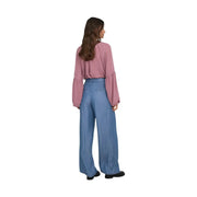 Eine Frau trägt eine weit geschnittene blaue Lyocell-Hose von Jacqueline De Yong mit einer hellrosa Bluse und ausgestellten Ärmeln.