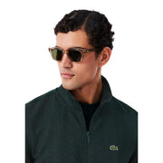 Braune Lacoste-Sonnenbrille mit Acetatrahmen und dunkelgrünen rechteckigen Gläsern, kombiniert mit einem grünen Baumwoll-Hoodie.