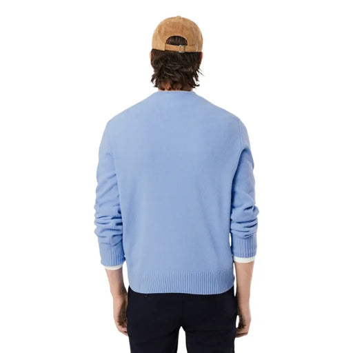 Hellblauer Lacoste Herren-Strickpullover aus Wolle mit Rundhalsausschnitt, gerippten Bündchen und Saum, kombiniert mit einer hellbraunen Cordmütze.