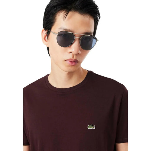 Silberfarbene Pilotenbrille mit dunkelgrauen Gläsern, kombiniert mit einem bordeauxroten Baumwoll-T-Shirt von Lacoste für Herren.