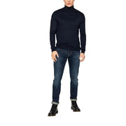 Ein Mann trägt eine blaue Levi's Herrenjeans aus Baumwollstretch, reguläre Passform (Modell 04511-1390), kombiniert mit einem marineblauen Rollkragenpullover.