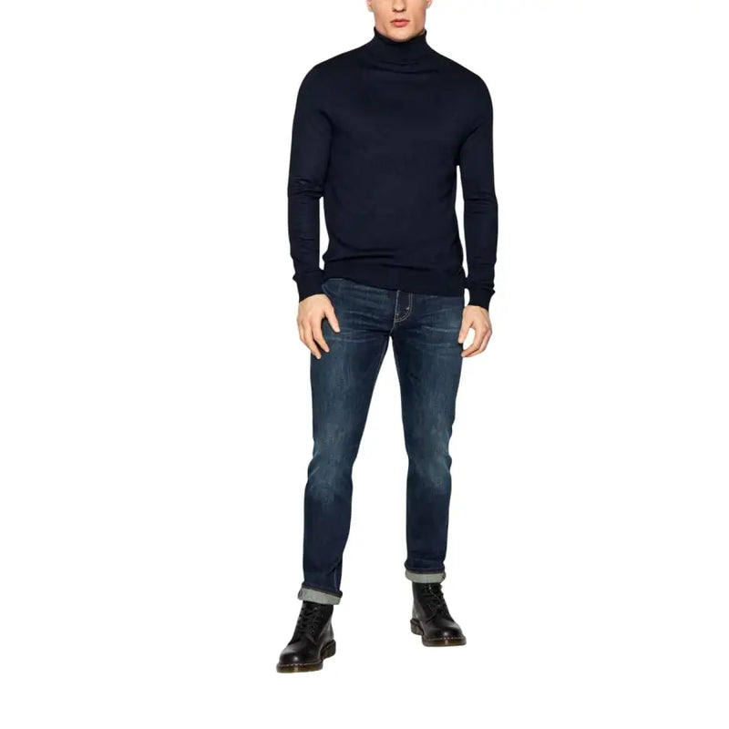 Ein Mann trägt eine blaue Levi's Herrenjeans aus Baumwollstretch, reguläre Passform (Modell 04511-1390), kombiniert mit einem marineblauen Rollkragenpullover.