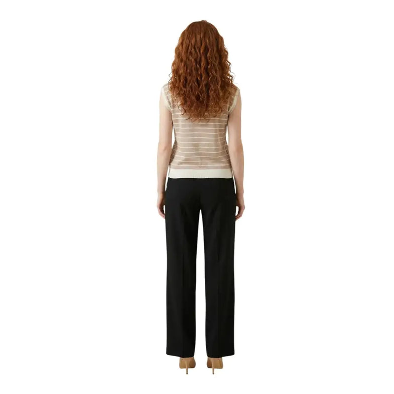 A woman wearing a liu jo beige striped sleeveless v neck sheer blouse with a solid white hem and black trousers