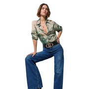 Eine Frau trägt Liu Jo Damen-Jeans aus blauem Baumwoll-Stretch mit weitem Bein, kombiniert mit einer grünen Seidenbluse mit Blumenmuster und einem schwarzen Gürtel