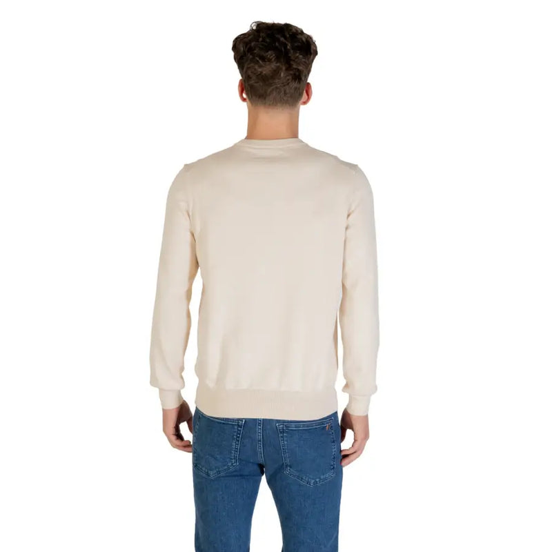 Man wearing a beige crewneck sweater and blue jeans, showcasing men’s casual fashion