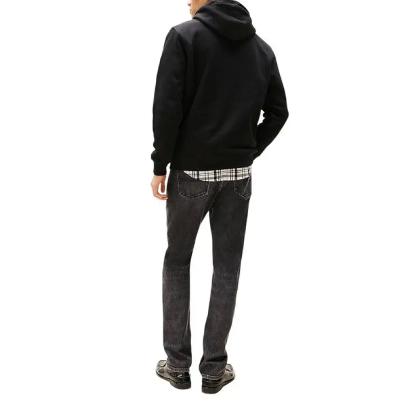 Man wearing a black hooded sweatshirt and jeans, showcasing casual men’s fashion