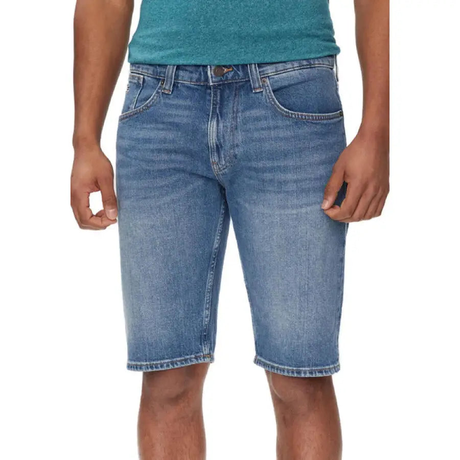 
                      
                        Man modeling Tommy Hilfiger jeans in green shirt and blue shorts
                      
                    