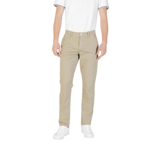 Ein Mann trägt beigefarbene Hosen mit Reißverschluss und Knopfverschluss, dazu weiße Turnschuhe.
