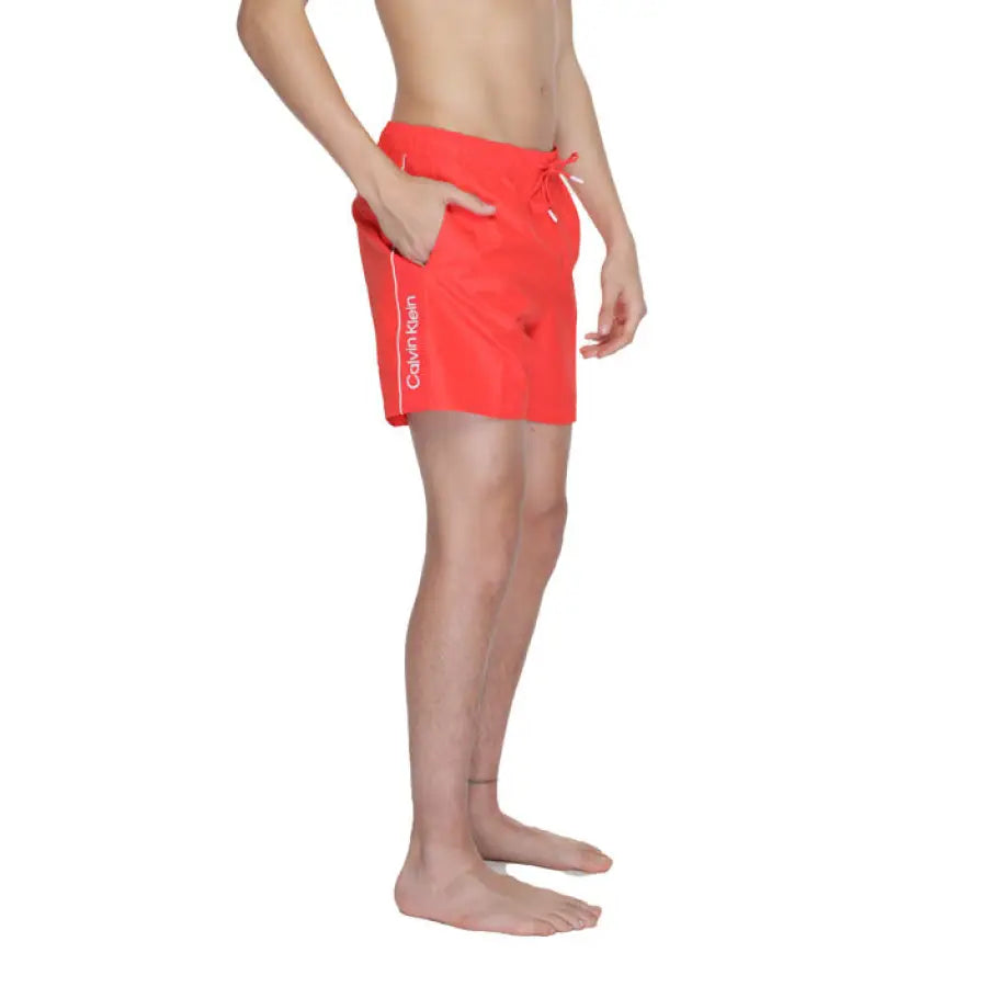 
                      
                        Man in Calvin Klein red swim trunks posing with hands on hips
                      
                    