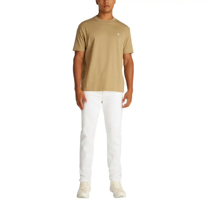 Man wearing a tan T shirt and white denim jeans showcasing men’s casual fashion
