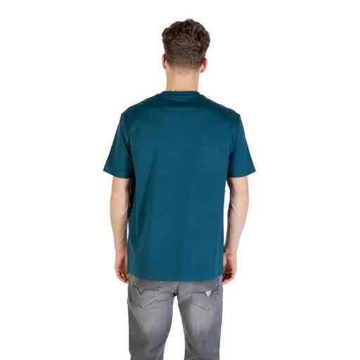 Man wearing a teal crew neck T shirt and gray jeans, showcasing men’s casual fashion