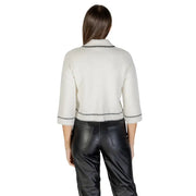 Woman wearing off-white fuzzy cropped cardigan with black trim and black faux leather pants