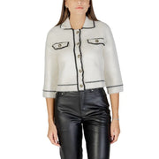 Woman wearing a white cropped cardigan with black trim over black leather pants