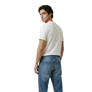 Ein Mann, der ein schlichtes weißes kurzärmeliges Baumwollhemd trägt. t-shirt und mittelblaue Jeans von New Balance