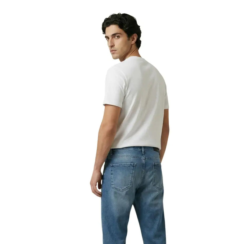 Ein Mann, der ein schlichtes weißes kurzärmeliges Baumwollhemd trägt. t-shirt und mittelblaue Jeans von New Balance