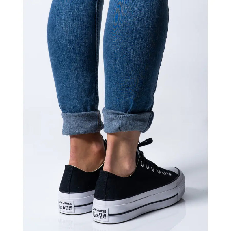 Woman wearing blue jeans and black Converse platform sneakers in product image