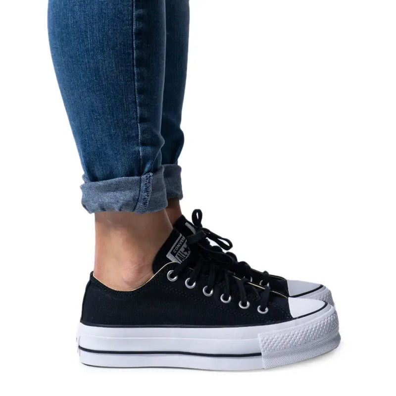 Lower legs and feet wearing cuffed blue jeans and black platform Converse sneakers