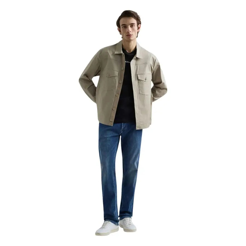 Beige Utility-Jacke mit Knopfleiste und zwei Brusttaschen, kombiniert mit blauen Stretch-Jeans von Replay Men mit geradem Bein.