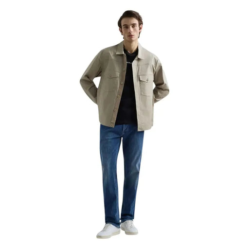 Beige Utility-Jacke mit Knopfleiste und zwei Brusttaschen, kombiniert mit blauen Stretch-Jeans von Replay Men mit geradem Bein.