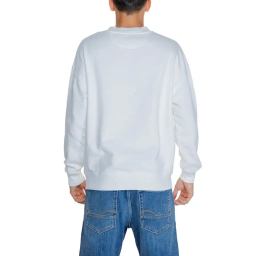 Person from behind wearing a white long-sleeve crewneck sweatshirt and blue jeans