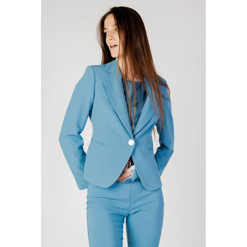 A woman wears a tailored rinascimento turquoise blazer with a single white button and matching slim-fit trousers