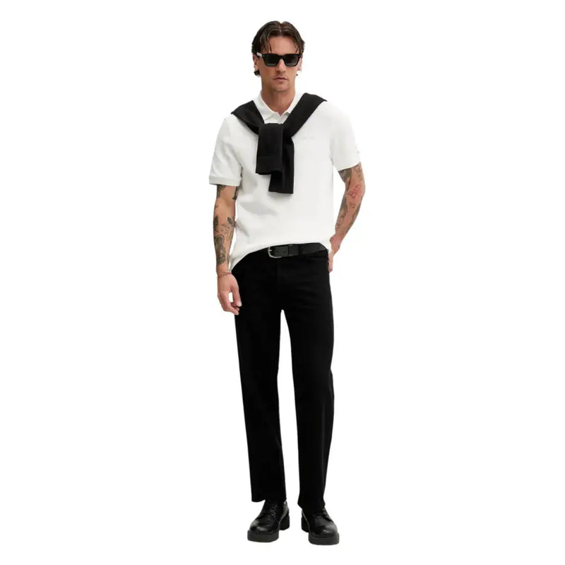 Ein Mann, der ein weißes, kurzärmeliges Poloshirt mit schwarzer Krawatte, Tommy Hilfiger Jeans und einen schwarzen Baumwollstrickpullover trägt.