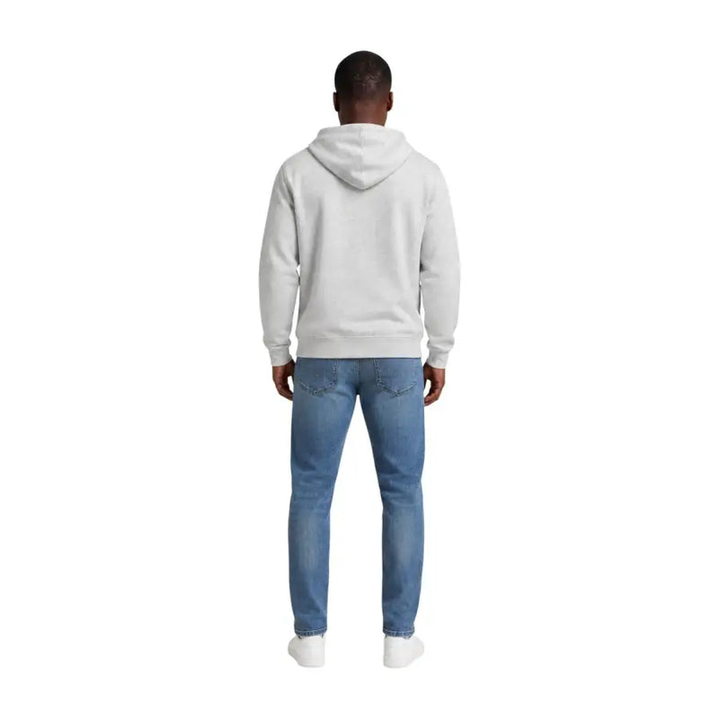Ein Mann, der einen grauen Hoodie aus Bio-Baumwolle und blaue Jeans trägt Tommy Hilfiger Jeans Herrenkollektion