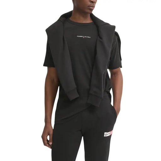 Black tommy hilfiger jeans hoodie draped over matching black t shirt and pants with subtle white chest branding