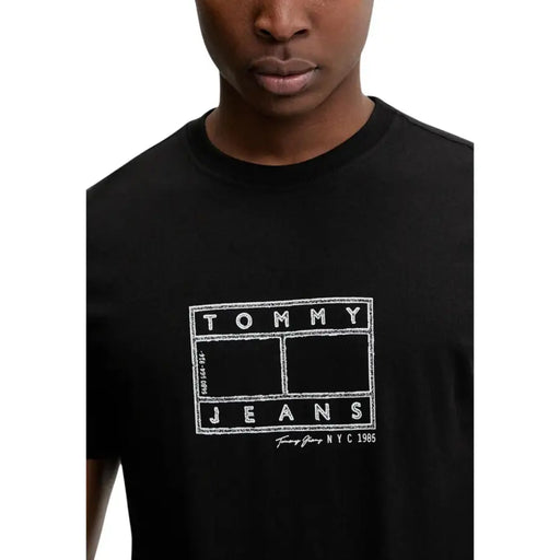 Schwarz Tommy Hilfiger Herrenjeans t-shirt mit weißem Tommy Jeans NYC 1985 Logo im Kreidestil auf der Vorderseite