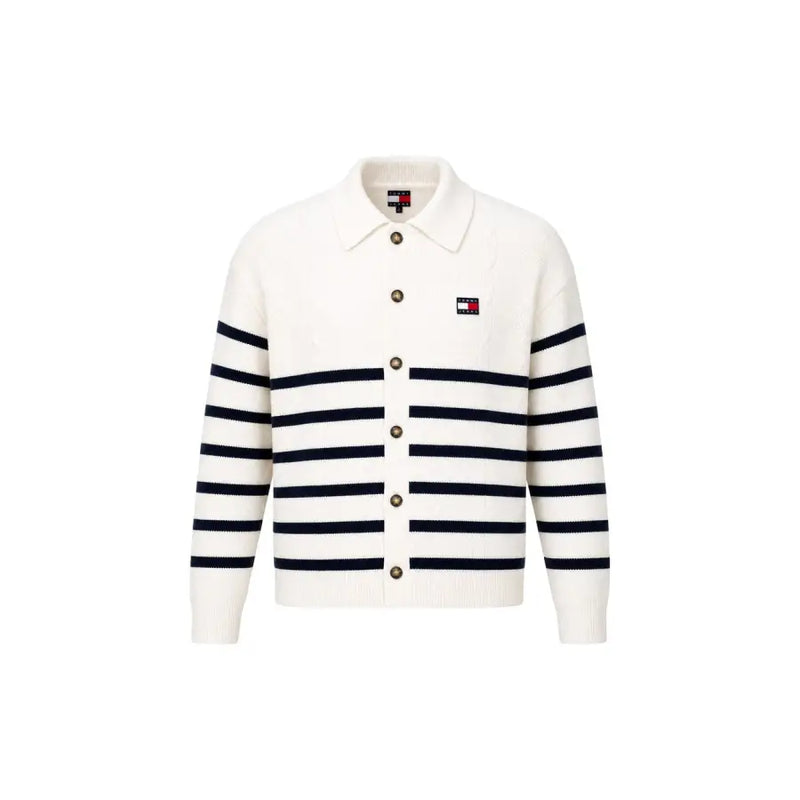Eine cremefarbene Strickjacke mit marineblauen Streifen und Knopfverschluss, kombiniert mit einem weißen Bio-Baumwoll-Sweatshirt von Tommy Hilfiger für Herren.