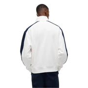 Weiße Lacoste-Trainingsjacke mit marineblauen Kontrasteinsätzen an Ärmeln und Schultern, kombiniert mit einer weiß gestreiften Tommy Hilfiger Jeans und einem Sweatshirt aus Bio-Baumwolle.