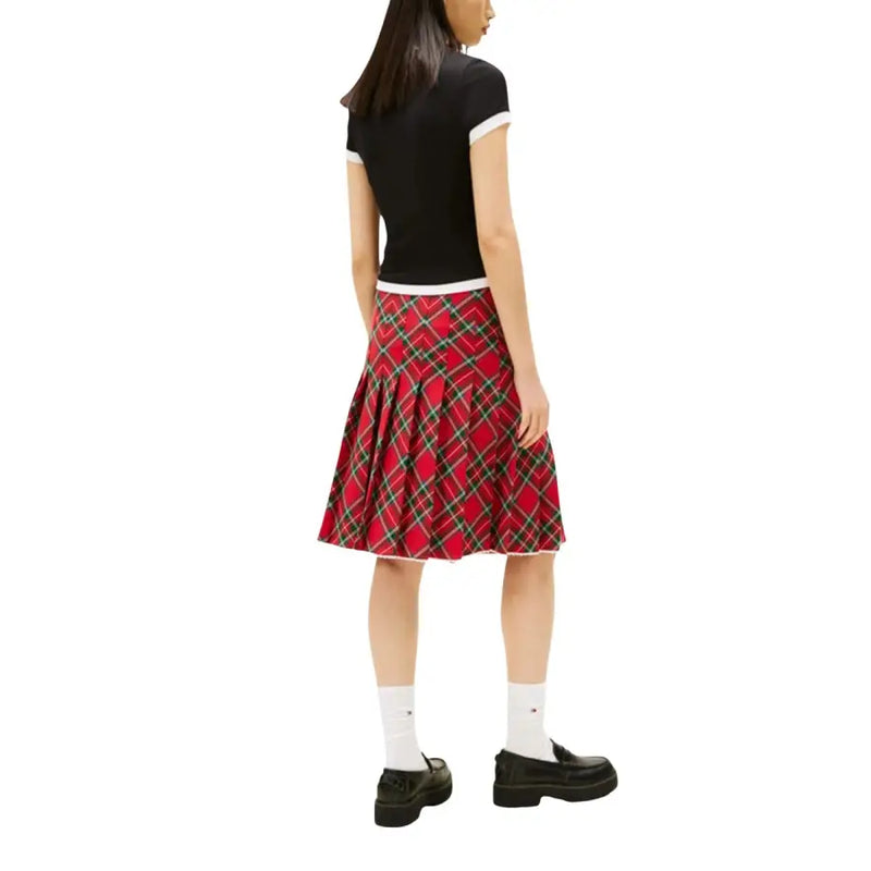 Roter Faltenrock mit Karomuster und schwarzen sowie grünen Akzenten, kombiniert mit einer schwarzen Tommy Hilfiger Jeans aus Bio-Baumwolle für Damen. t-shirt