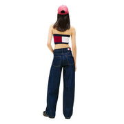 Eine Frau, die dunkelblaue, weit geschnittene Tommy Hilfiger Jeans aus Bio-Baumwolle mit Logo am hinteren Bund und eine pinkfarbene Kappe trägt.