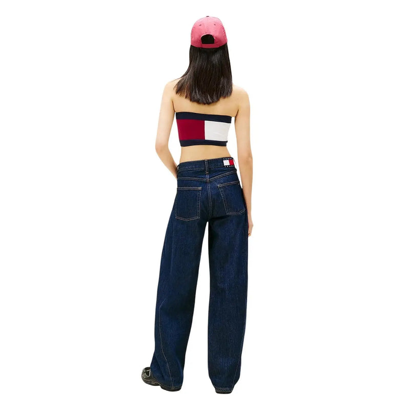 Eine Frau, die dunkelblaue, weit geschnittene Tommy Hilfiger Jeans aus Bio-Baumwolle mit Logo am hinteren Bund und eine pinkfarbene Kappe trägt.