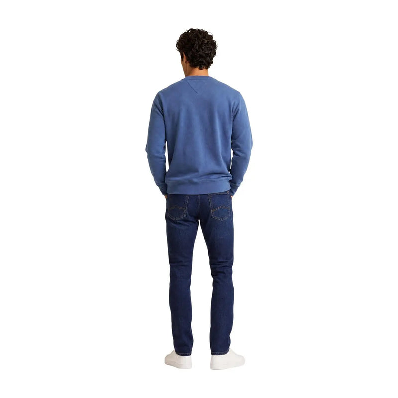 Ein Mann, der einen Tommy Hilfiger Herren-Sweatshirt aus blauer Baumwolle mit Rundhalsausschnitt und dunkelblauer Jeans