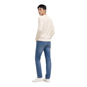 A man wearing a cream-colored Tommy Hilfiger white round neck knit sweater made from organic cotton paired with blue jeans