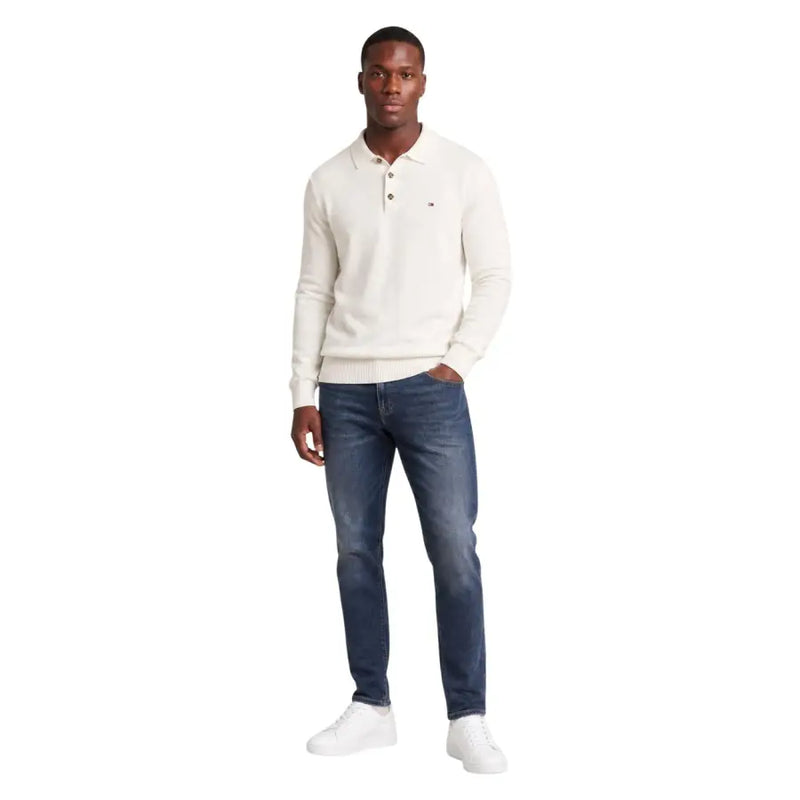 Cremefarbener Tommy Hilfiger Polopullover mit klassischem Kragen und Knopfleiste, kombiniert mit einer schmal geschnittenen blauen Baumwolljeans.