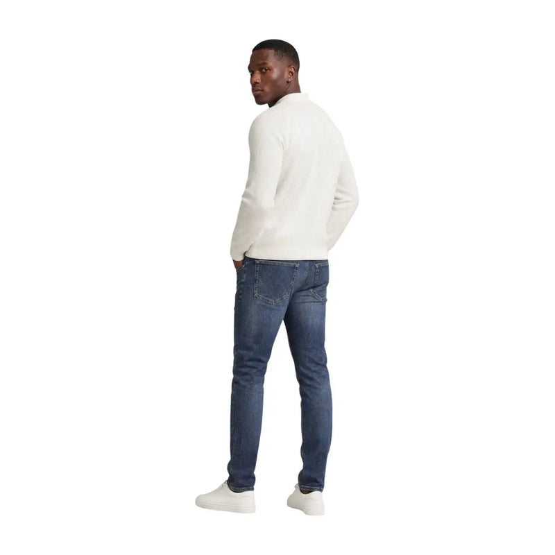 A man wearing tommy hilfiger men scanton slim blue jeans cotton paired with a cream-colored long-sleeved knit sweater