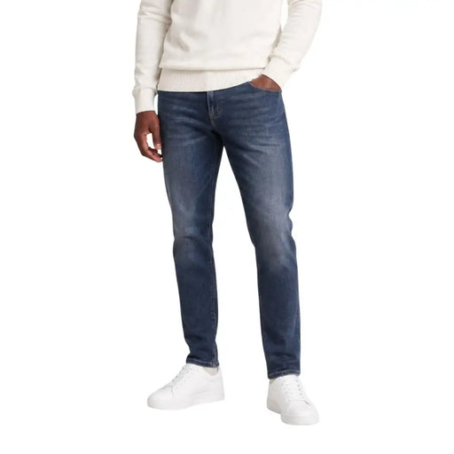 Tommy Hilfiger Herren Scanton Slim-Jeans aus blauer Baumwolle mit dunkler Waschung und dezenten Ausbleichungen, getragen von einem Model in Freizeitkleidung