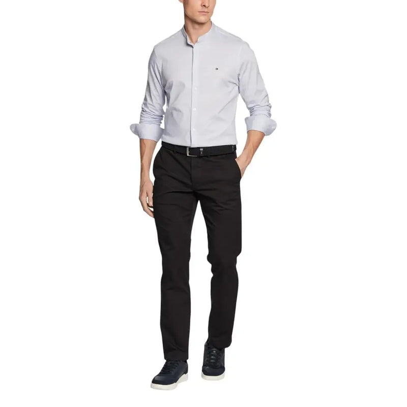 Hellgraues Tommy Hilfiger Herrenhemd mit hochgekrempelten Ärmeln und dezentem Logo auf der Brust, kombiniert mit einer Hose.