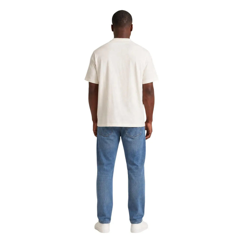 Ein Mann, der einen cremefarbenen Tommy Hilfiger Weißes, kurzärmeliges Bio-Baumwoll-T-Shirt für Herren mit blauer Jeans