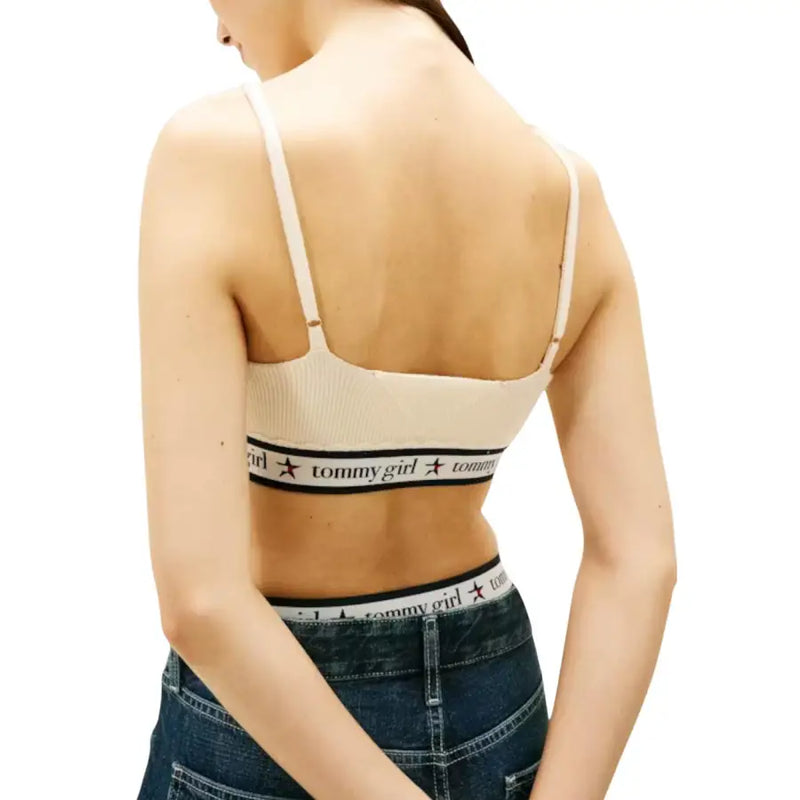 Beige ribbed tommy girl bra with thin straps and black elastic band featuring tommy hilfiger logo under white sleeveless v neck knit top for women