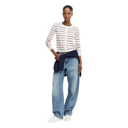 Eine Frau trägt eine weiße, langärmelige Strickjacke aus Bio-Baumwolle von Tommy Hilfiger mit roten und schwarzen Streifen.