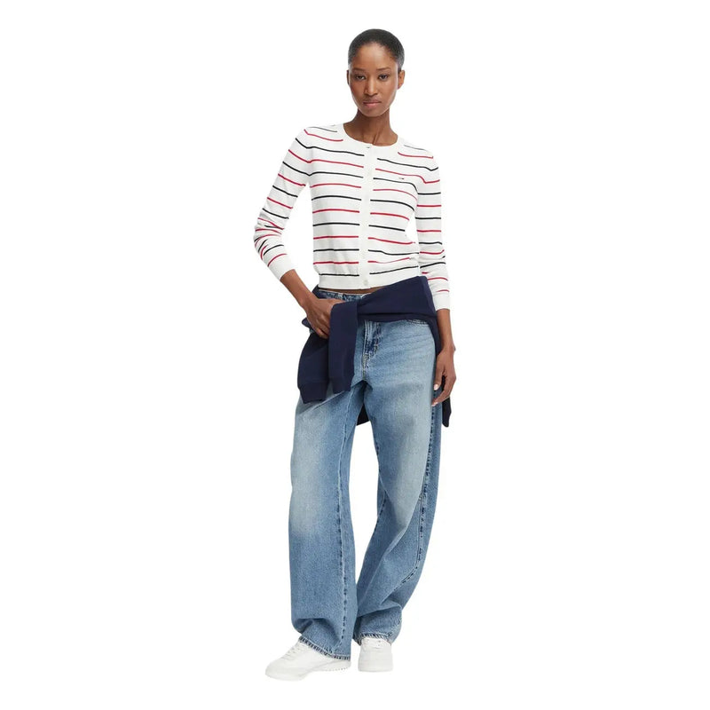 Eine Frau trägt eine weiße, langärmelige Strickjacke aus Bio-Baumwolle von Tommy Hilfiger mit roten und schwarzen Streifen.